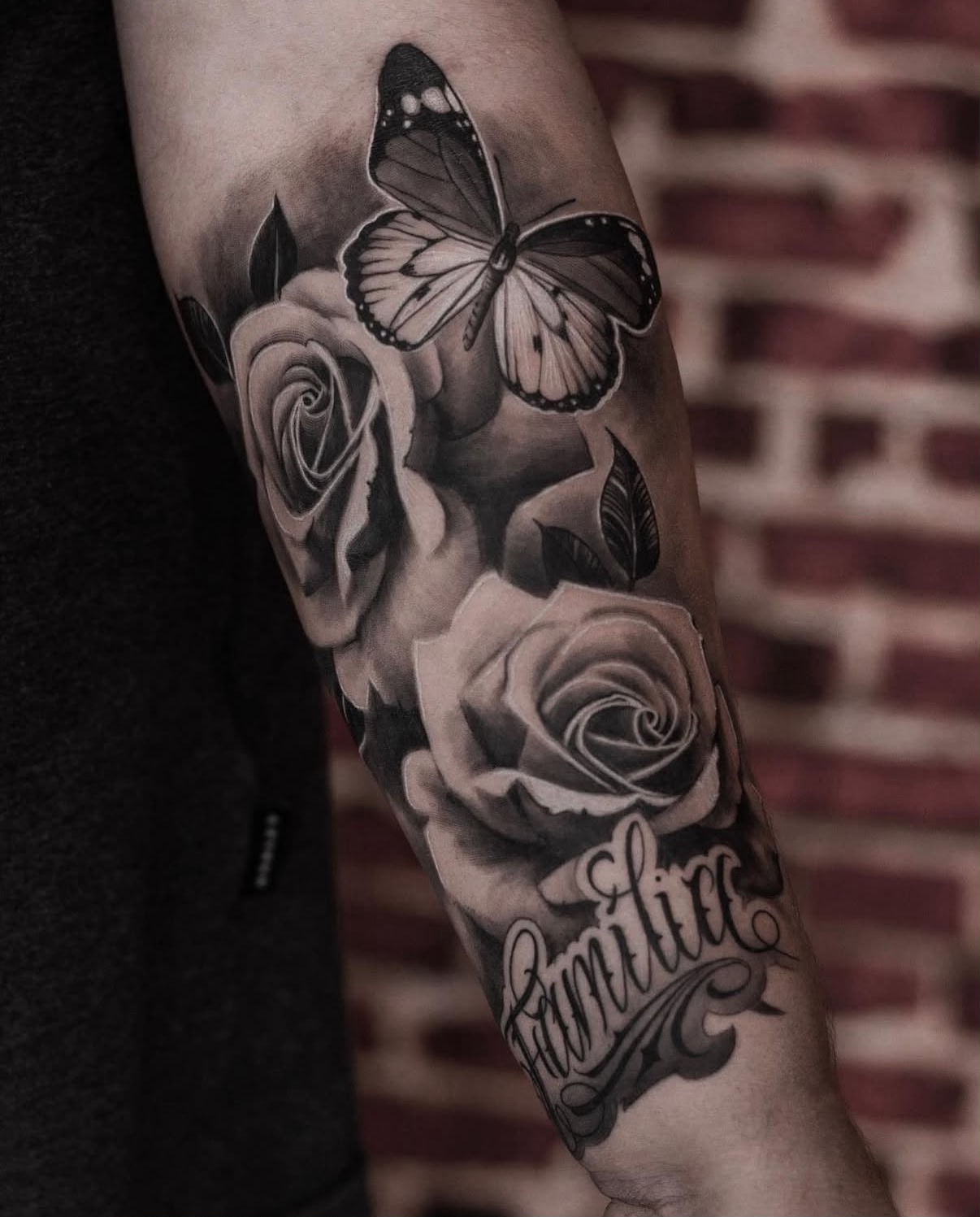 Antebraço com duas rosas, borboleta e lettering Família, realismo em preto e cinza por Felipe Carlos.