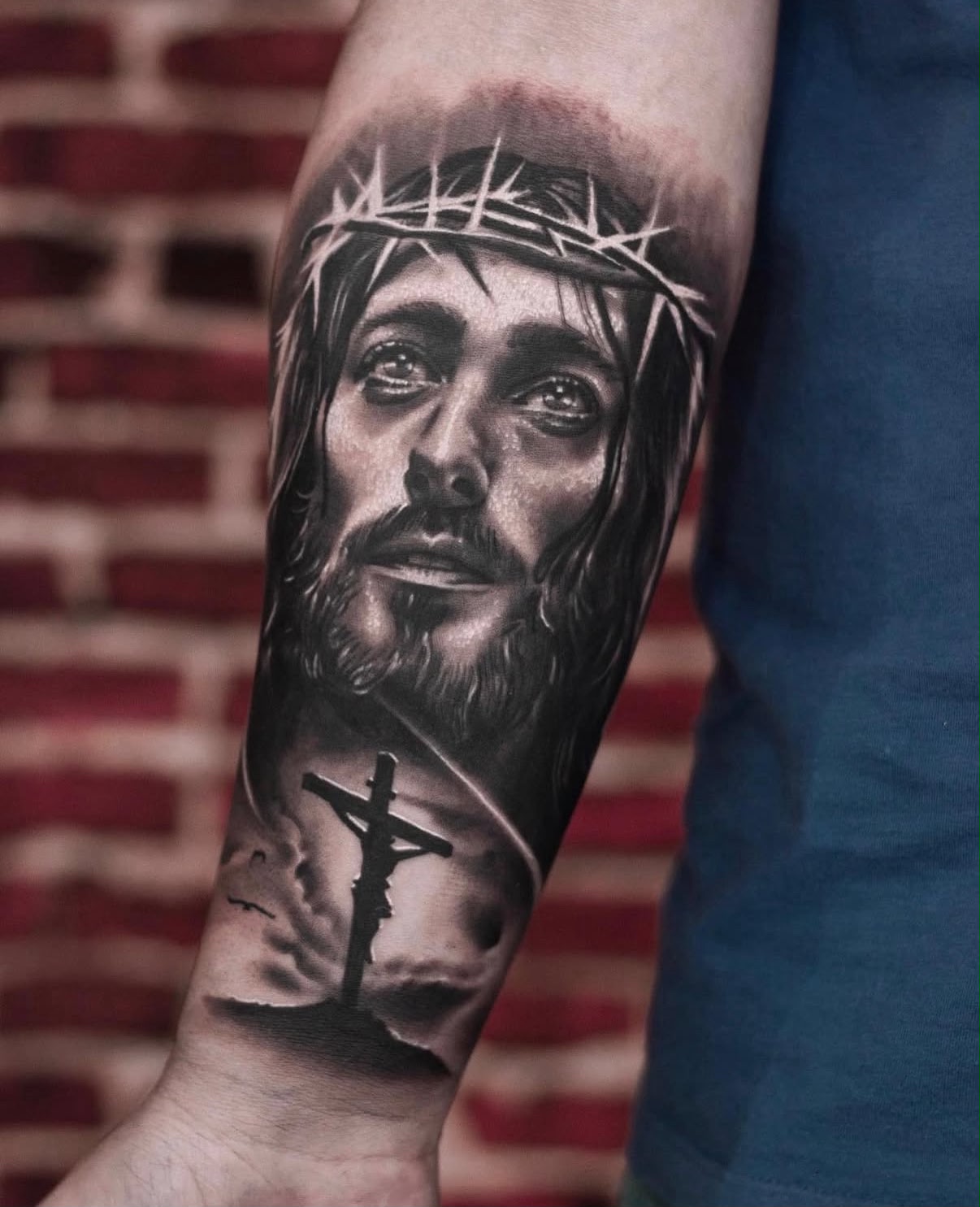 Antebraço com a face de Cristo coroado de espinhos sobre o calvário ao entardecer, realismo religioso em preto e cinza por Felipe Carlos.