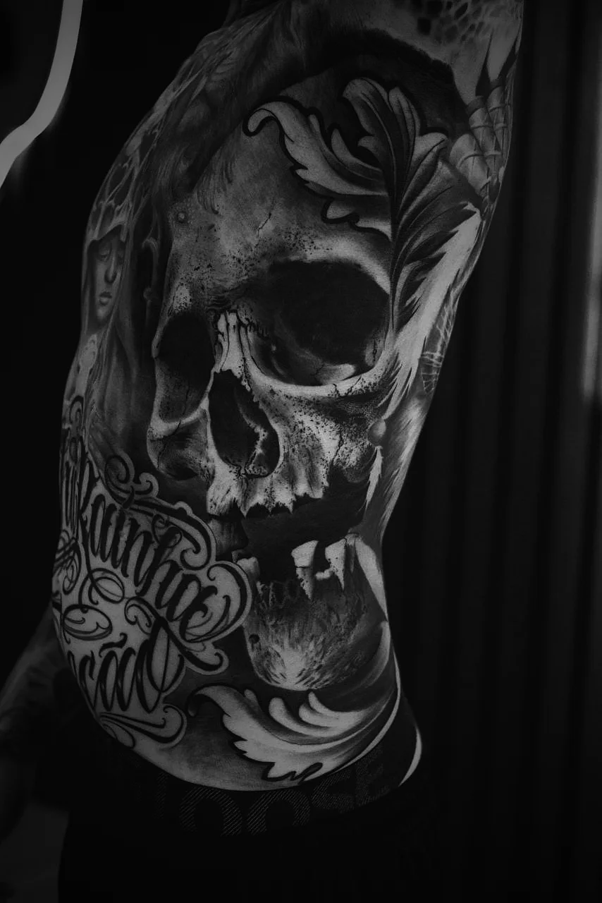 Costela fechada com crânio, ornamentos em acanto e lettering, realismo em preto e cinza por Felipe Carlos.